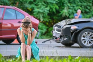 A woman sitting on a curb after a crash and wondering what to do after a car accident.