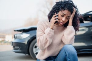 Woman on the phone near a crashed car calls to ask what to do after a truck accident.