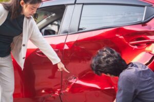 A woman pointing at damage to her car after a crash. A lawyer can explain what happens if someone else drives your car and gets in an accident.