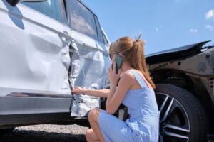 A photo of a woman checking her car after a car accident. Is it worth hiring an attorney for a car accident? 