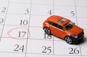 Calendar graphic next to a toy car sitting on a clipboard with financial documents to symbolize the question of how long car accident settlements take in WA.
